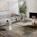 Bowery Storm Taupe Rug placed in modern living room with light gray sofa, fireplace, and natural plant