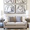 Set of four framed Black Circles IV paintings with bold black circular lines on white background, arranged above a sofa