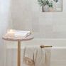 Throw hanging over edge of white bathtub with small side table holding candle and book