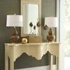 Single gold hammered ball sits on a cream table between brown lamps and a tall mirror in natural light