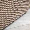 Close-up of weathered tobacco wicker texture and small logo tag near sofa base on concrete floor