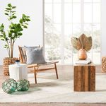 Lifestyle view of natural ivory rug in room with wooden chair, blue pillow, and woven plant basket