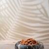 Brown Emperador marble bowl filled with almonds on wooden surface with soft leaf shadow background