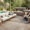 Rug styled outdoors under a pergola with modern outdoor seating and a brick fireplace