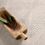 Close view of thick rug pile with carved medallion design beside a wooden bowl with leaves