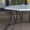 Close-up side angle of table base showing wrought aluminum curvature and faux stone top texture indoors