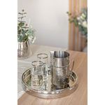Tray styled on wooden table holding a hammered silver pitcher and two clear glasses with water