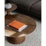 Close-up of orange book and white vase on the round coffee table showcasing the wooden surface grain