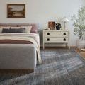 Charcoal rug shown in a bedroom setting under a gray upholstered bed with soft pink and gray bedding