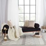 Rug visible under chaise lounge with dark upholstery and white knit throw in bright room