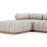 Side angle of light grey sectional showing deep tufting, rounded edges, and teak base with ottoman