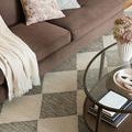 Close-up detail of rug beside brown sofa and glass coffee table showing wool texture and striped diamond pattern