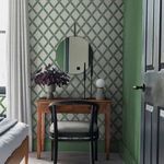 Room context showing Greenskeeper wallpaper on wall behind wooden vanity, green painted wall, and black door