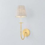 Amina Wall Sconce with aged brass finish, slender J-arm, white candle sleeve, and white linen shade