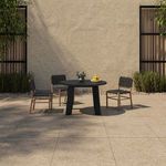 Outdoor patio scene with round black dining table and four matching black strap chairs against textured stone wall