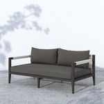 Outdoor Sherwood sofa with vertical woven strap back shown outdoors against pale wall with shadows.