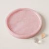Side angled view of pink alabaster tray with small decorative glass sphere and dried petal