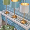 Three Mirasol lamps in white, blue, and green arranged on white console with blue wall background