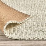 Corner of jute rug flipped over revealing non-slip brown backing material