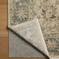 Corner of rug lifted to reveal non-slip rug pad underneath on hardwood floor