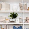 Colanders stacked and styled on a white shelf alongside decorative pillows, plants, and woven baskets