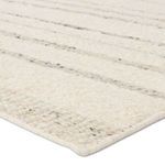 Close-up angled view showing textured wool pile and woven edge of striped cream and taupe rug