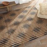 Close angled view of rug corner with pillows and sunlight on wooden floor