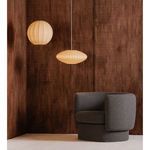 Lys Pendant and round pendant lamp in warm light next to a grey armchair with brown wooden wall