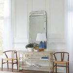 Tupelo lamp on console table flanked by wooden chairs in bright room with tall mirror and white walls