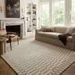 Bradley Ivory / Beige Rug in living room with sofa, armchair, and large windows providing natural light