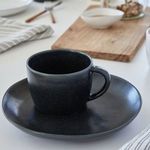 Matching matte black cup placed on the plate, displayed on a bright kitchen countertop