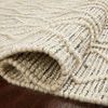 Side view of Noelle rug slightly rolled to show thickness and woven pattern on dark floor