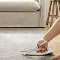 Hand cutting beige rug pad with white-handled scissors on hardwood floor near sofa