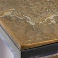 Close-up of antique brass cast aluminum tabletop with textured, drift-like finish and black iron leg corner