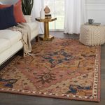 Dark pink and blue medallion rug styled in a living room with sofa, ottoman, and natural light