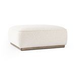 Side angled view of ottoman showing plush seat cushion and wood base