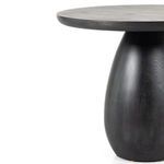 Black wash end table topped with wood candle holder and dried floral arrangement next to sofa