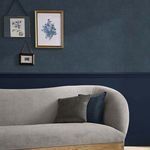Haptic navy wallpaper applied on a wall behind a grey curved sofa with pillows and framed floral art