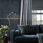 Salix Leaves Wallpaper shown in a living room setting behind a blue sofa with curtains and a floor lamp