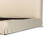 Angle view of cream linen slipcovered bed frame showing pleated skirt