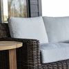 Side detail of light gray cushions with woven resin wicker armrest beside wooden side table on porch