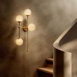 Armstrong 4 L Sconce lit, mounted beside wooden stairs with textured beige wall and curved banister