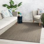 Rug styled in light room with wicker sofas, patterned pillows, and plants