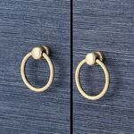 Close-up of two round metal ring pull handles in a muted gold finish