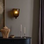 Lit Cerie Sconce mounted on wall above black sideboard with decorative objects in room setting