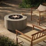 Fire table in outdoor patio setting with chair and greenery, flames visible to evoke ambiance