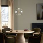 View of clear glass globe pendant light in dining room with beige curtains and decorative table setting