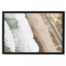 Aerial seaside photograph showing a lone surfer waiting to paddle out, waves crashing on sandy beach near railway track