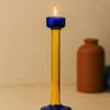 Single lit candle inside holder, warm neutral background with blurred brown vase