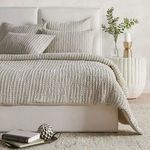 Styled bedroom setting with multiple shams and matching bedding on white upholstered bed, side table decor